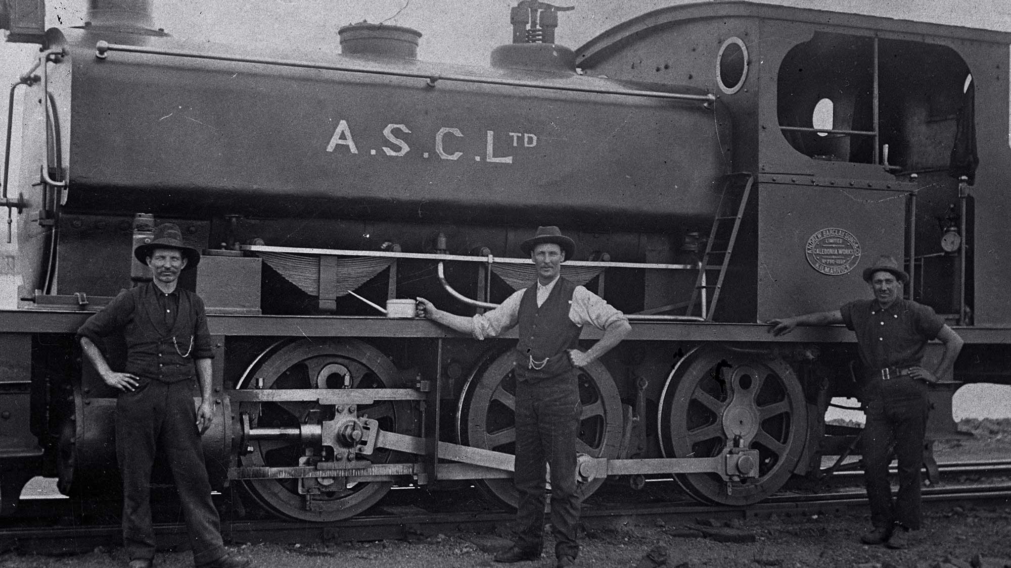 Historical photo of three men standing in front of a train car.